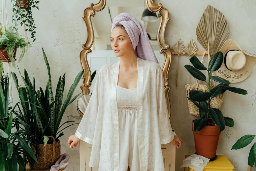 a woman in a white robe or towel, looking confident and comfortable in a bright, spa-like setting.