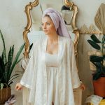 a woman in a white robe or towel, looking confident and comfortable in a bright, spa-like setting.